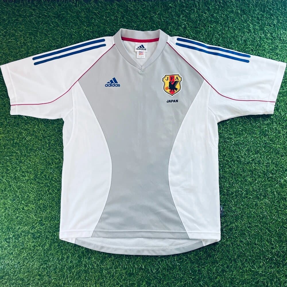 Japan 2002 away shirt, front: white with blue adidas shoulder stripes, red and blue trim, a V-neck and the JFA crest.
