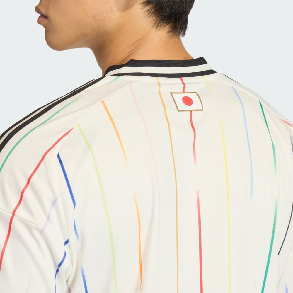Back-neckline detail of the Japan 2026 away shirt worn on-body: the gold-bordered Hinomaru flag tab, the black collar and shoulder Three Stripes, and the fading multicolor pinstripes.