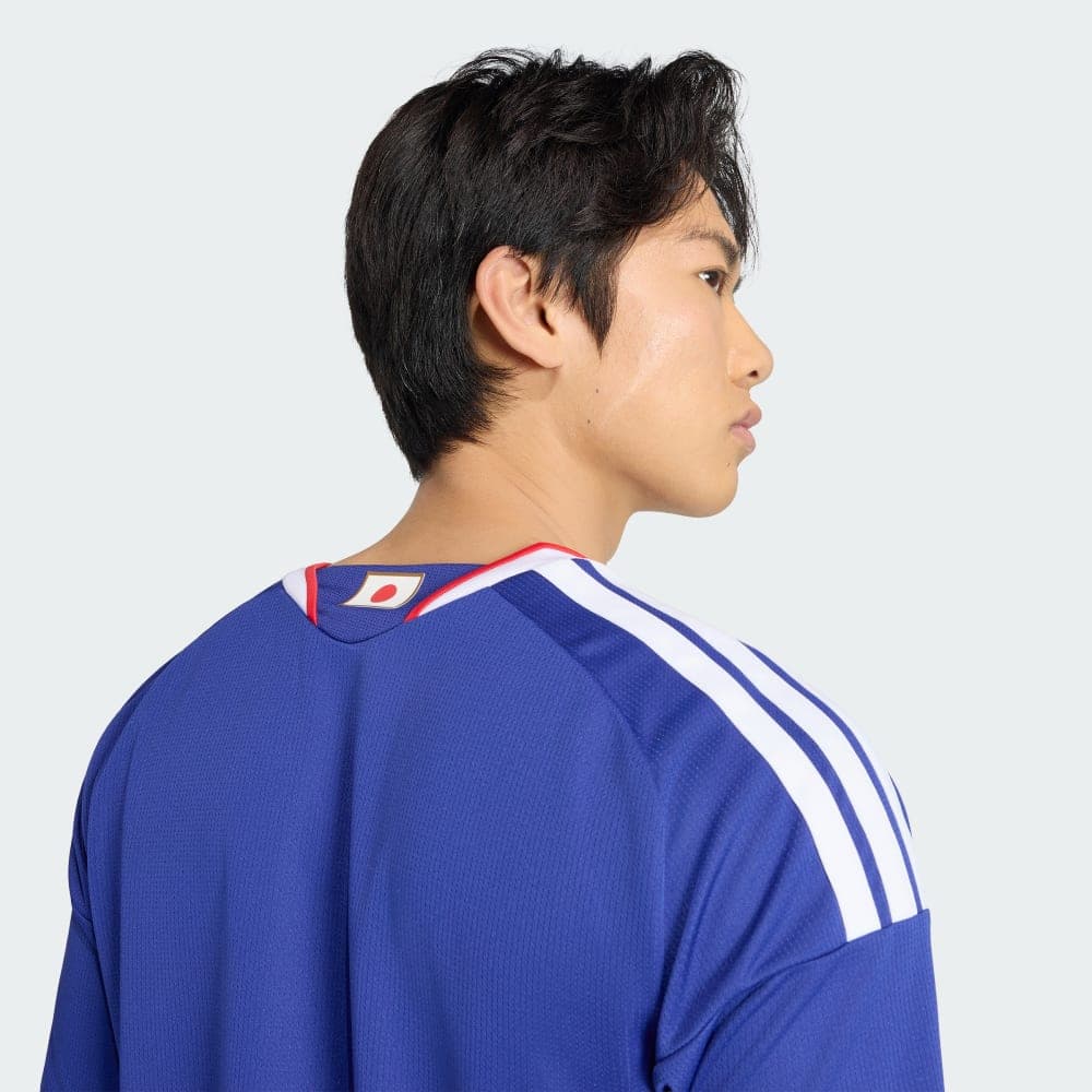 Collar detail of the Japan 2026 home shirt worn on-body: the Hinomaru tab at the back of the neck and the white adidas Three Stripes running over the shoulder.